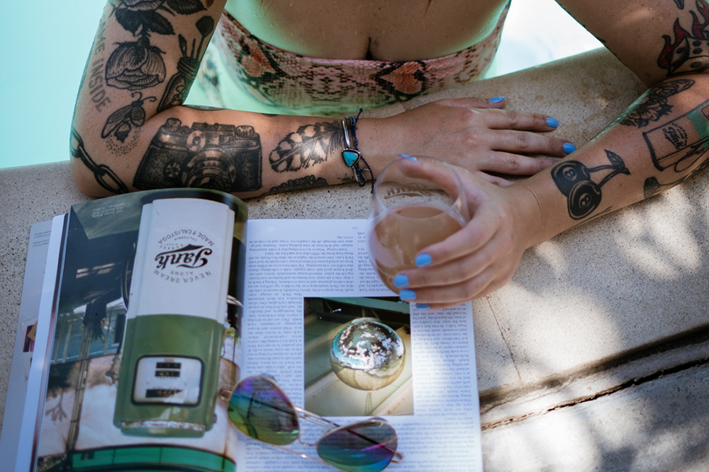 person in pool reading tank article in magazine with wine glass