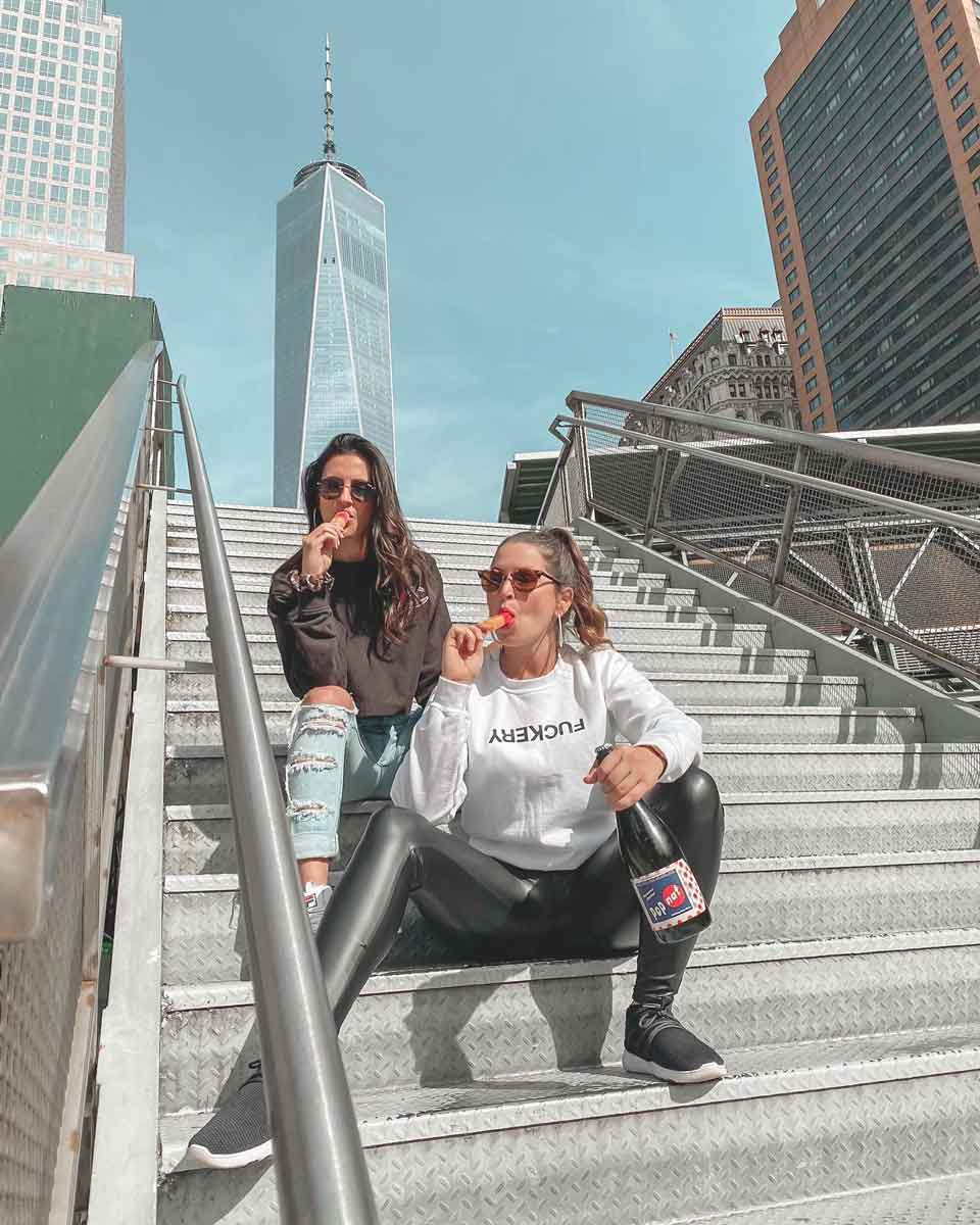 Two women sitting on a staircase in New York City holding a bottle of Pop Nat